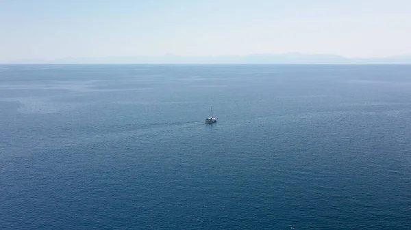 Incredible aerial shot in the open sea with a view of a white boat sailing in Aegean Sea, Greece. Stock Image