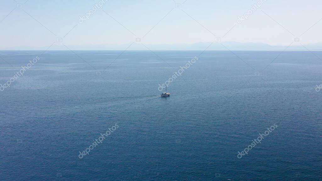 Incredible aerial shot in the open sea with a view of a white boat sailing in Aegean Sea, Greece.
