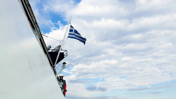 에게 해에 있는 뱃머리 뒤에서 구름낀 하늘을 향해 흔들리고 있는 그리스 국기. — 스톡 사진