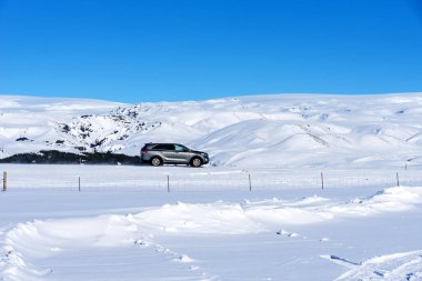 Tipik İzlanda kış manzarası. Kar altında dağlar ve mavi gökyüzü. Dağlı güzel kış manzarası, soğuk soğuk hava ve asfalt yolu İzlanda 'da arabalı beyaz bir arazide..
