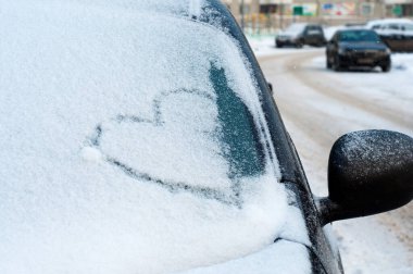 Kışın arabanın camına kalp çizilmiş. Kışın araba camındaki karda yakın plan kalp çizimi..