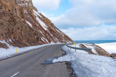 İzlanda 'nın Atlantik Okyanusu kıyısındaki Route 1' in panoramik manzarası. Kış mevsiminde İzlanda 'da dağ ve okyanusla çevrili ve karla kaplı kıvrımlı yol..