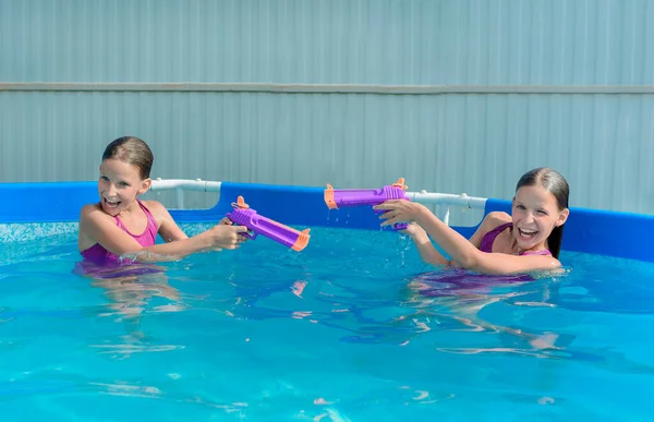 Two tween caucasian girls with water guns toy fight game in pool —  Fotos de Stock