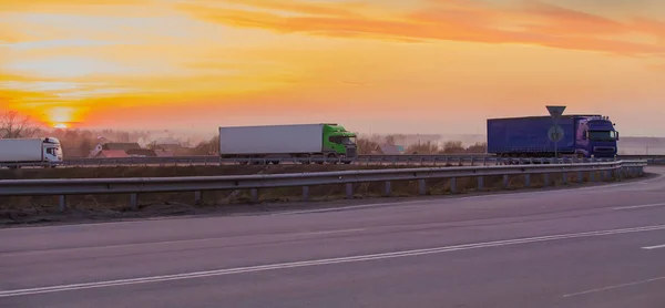 Trucks move at sunset on a suburban highway at a road junction along the village