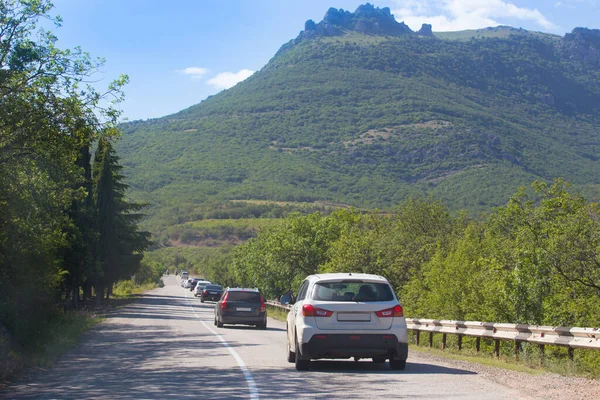 Cars move along a winding mountain road on a summer day