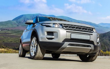 SUV bir dağ manzarasının arka planında yolda ilerliyor