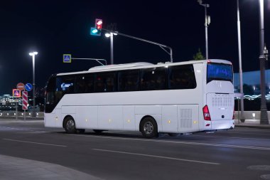 Turist otobüsü aydınlık şehir caddesinde gece hareket ediyor.