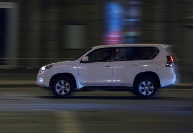 SUV gece şehir caddesinde hareket ediyor.