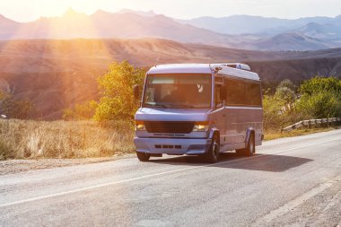 Kamu minibüsü, dağ arkaplanına karşı yol boyunca sürüş yapıyor.