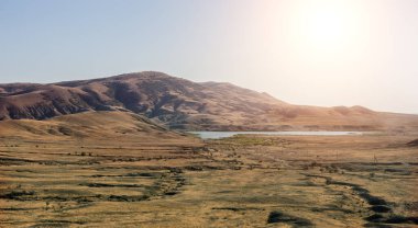 Güneşle aydınlatılan dağ sırasının yakınında gölü olan güzel bir manzara vadisi.