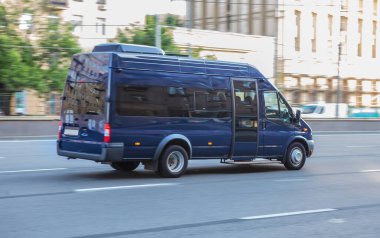 Minibüs gün ışığıyla aydınlatılmış bir cadde boyunca ilerliyor.