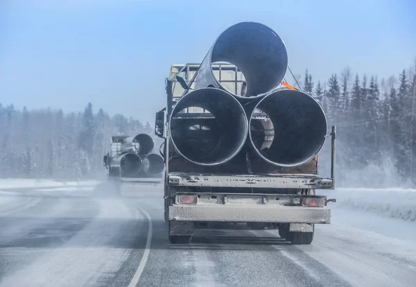 truck transports large-diameter pipes for a gas pipeline on a winter snow-covered road.