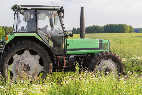 Agricultural tractor moves through the meadow in summer