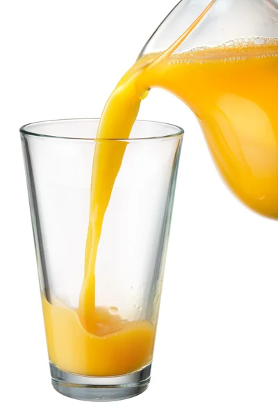 O suco de laranja é derramado do jarro no copo — Fotografia de Stock