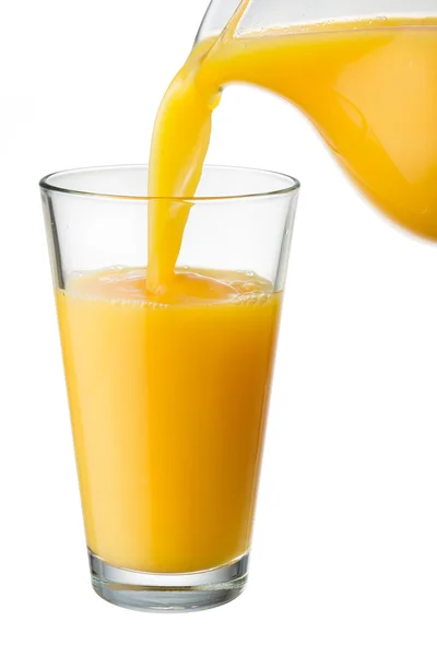 O suco de laranja é derramado do jarro no copo — Fotografia de Stock