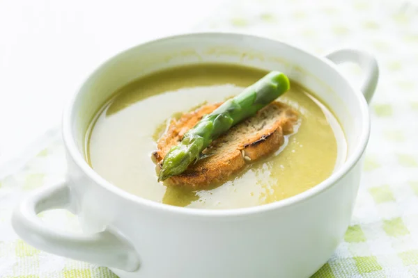 Bowl of asparagus soup with asparagus spear and bread on cutting board — Stock Photo, Image