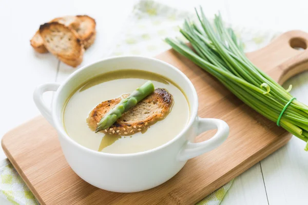 Bowl of asparagus soup with asparagus spear and bread on cutting board — Stock Photo, Image