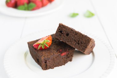 Çikolatalı browni kek beyaz tabakta strawberrie ile dekore edilmiştir.