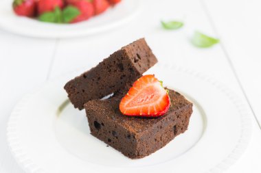 Çikolatalı browni kek beyaz tabakta strawberrie ile dekore edilmiştir.