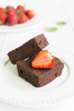 Çikolatalı browni kek beyaz tabakta strawberrie ile dekore edilmiştir.