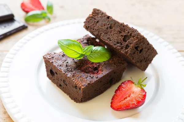 Çikolatalı browni kek beyaz tabakta strawberrie ile dekore edilmiştir.