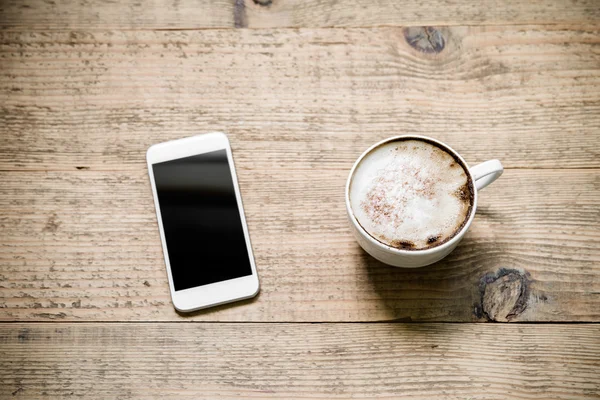 Kopp kaffe latte med vita smartphone på träbord — Stockfoto