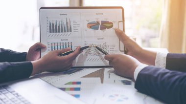 İş belgesi sunum özeti raporuna işaret eden iki iş adamının mali görüntüsü, toplantıda tartışılırken, ahşap masadaki defter