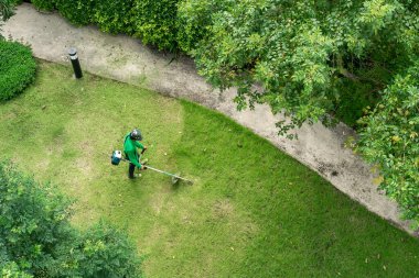 Çim biçme makinesiyle çim biçen bir işçi.