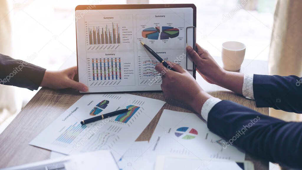 financial Image of two young business people pointing at business document during discussion at meeting , Notebook on wood table