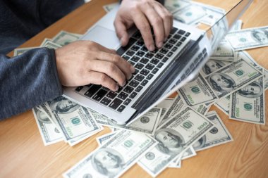 Üst düzey iş adamları iş için klavye bilgisayarında dizüstü bilgisayarla çalışıyor, ofis masasında dolarlarımız var.