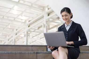 İş kadını kıyafetleriyle gülümseyen güzel kız dizüstü bilgisayar kullanıyor, şehir geçmişi var.