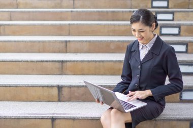 İş kadını kıyafetleriyle gülümseyen güzel kız dizüstü bilgisayar kullanıyor, şehir geçmişi var.