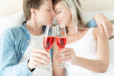 Yatak odasındaki yatakta bir kadeh şarap tutan genç çiftin seçici odak elleri birlikte romantik bir an kutluyorlar.