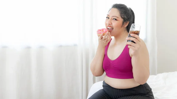 肖像画美しい若いアジアのふっくらした女性の喜びのジャンクフード 不健康な食べ物 甘い御馳走ケーキとコーラは あなたが脂肪である理由のベッドルームで甘い水を飲む 女性の食事量の損失が太りすぎ — ストック写真