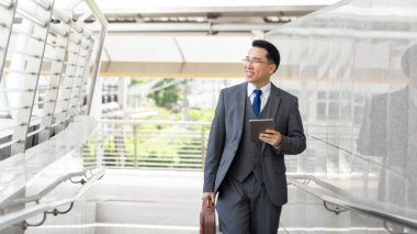 İş bölgesinde yürüyen Asyalı iş adamı portresi. İş görüşlü üst düzey yöneticiler. Elinde telefon bilgisayarı var.