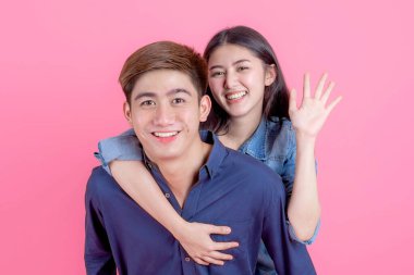 Genç adamın kız arkadaşını sırtında taşıdığı ve pembe arka planda gülümseyen kameraya baktığı portre genç çift konsepti