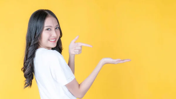 美しい若いですアジアの女性ポージング彼女の空の手とともにコピースペース 空白のスペースのために広告孤立した黄色の背景 — ストック写真