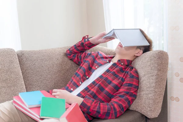 Asian young man sleeping on couch while stack of books placed on his body