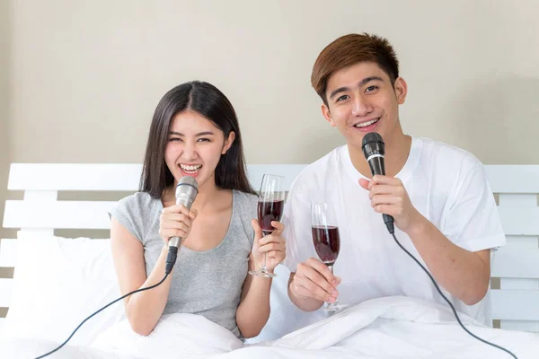 若いアジアのカップルはワインの幸せな保持ガラスを埋めると歌カラオケパーティーを歌うの寝室でお祝い — ストック写真