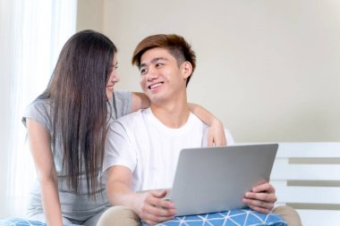 Mutlu, güzel bir kadın ve yakışıklı bir adam evdeki yatak odasındaki yatağın üzerinde dizüstü bilgisayar kullanıyor. Genç çift kavramı.