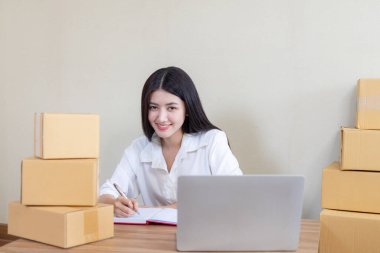 Güzel bir Asyalı iş kadını, e-posta siparişi ürününü aldıktan sonra mutlu oldu. Ev ofisinde bilgisayarla çalışan küçük bir işletme sahibi, teslimat için çevrimiçi pazar paketleme kutusu.