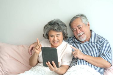 Tablet telefon kullanan üst düzey bir çift, akrabalarının torunlarına telefon ediyor. Gülümsüyor, evdeki koltukta mutlu oluyorlar. Son sınıf yaşam tarzı konsepti.