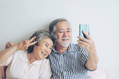 Akıllı bir telefon kullanan kıdemli çift, akrabalarının torunlarına telefon ediyor, gülümsüyor, sabah yatak odasında mutlu oluyorlar. Yaşlılar için yaşam tarzı konsepti.