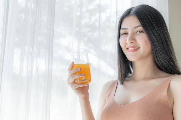 Beautiful beauty woman Asian cute girl feel happy drinking orange juice for good health in the morning , enjoying time in her home  white bedroom background - lifestyle beauty woman concept