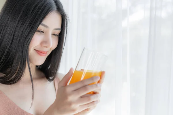 Beautiful beauty woman Asian cute girl feel happy drinking orange juice for good health in the morning , enjoying time in her home  white bedroom background - lifestyle beauty woman concept