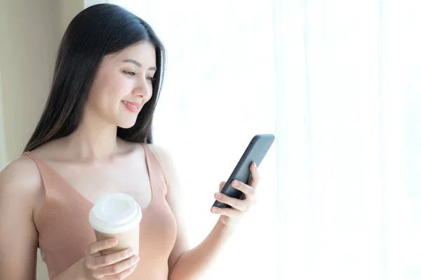 美しいかわいい女の子アジアの女性は 朝の白い寝室でスマートフォンを果たしています 家庭でのライフスタイル女性 — ストック写真