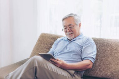 Akıllı telefon kullanan, gülümseyen, evdeki koltukta mutlu hisseden son sınıf öğrencisi. Yaşlılar konsepti.