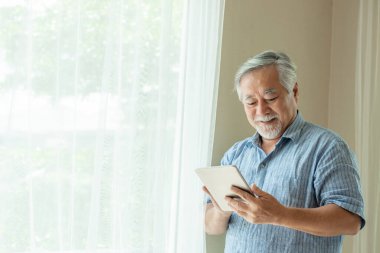 Akıllı telefon kullanan yaşlı bir erkek, gülümsüyor. Yatak odasında mutlu hissediyor. Son sınıf yaşam tarzı konsepti.