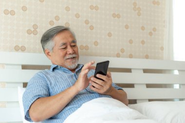 Akıllı telefon kullanan yaşlı bir erkek, gülümseyerek evde mutlu ol - yaşam tarzı son sınıf konsepti