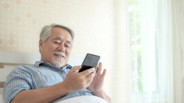 Akıllı telefon kullanan yaşlı bir erkek, gülümseyerek evde mutlu ol - yaşam tarzı son sınıf konsepti